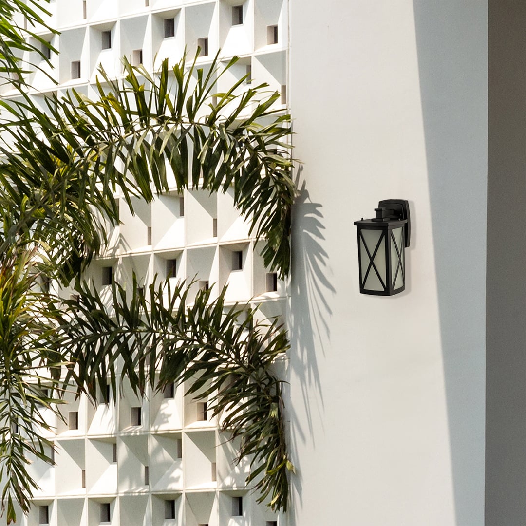 Black metal outdoor wall lantern lifestyle image with X frame overlay mounted on white modern villa wall by palm trees.