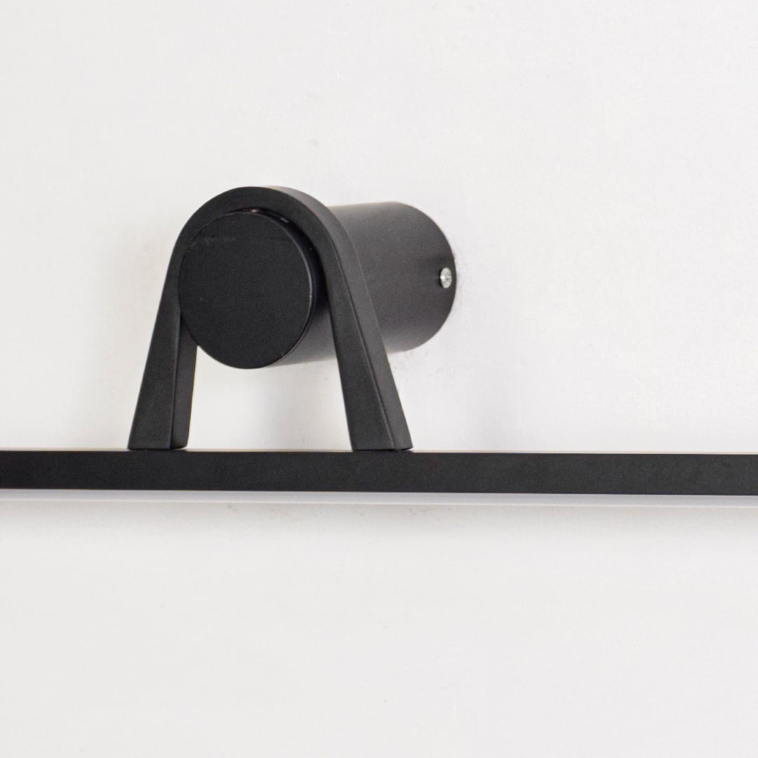 Closeup of black metal wall mounted picture light showcasing matte finish cylindrical base and minimalist linear bar.
