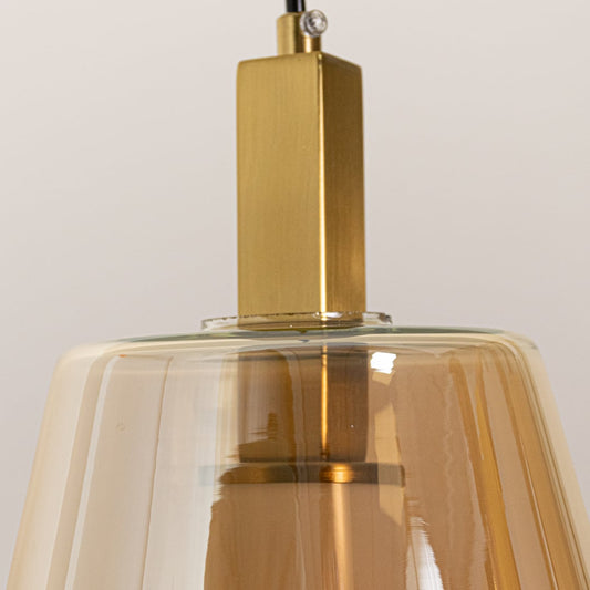 A closeup of the pendant light focusing on the gold metal top and the textured amber glass that gently reflects surrounding light.