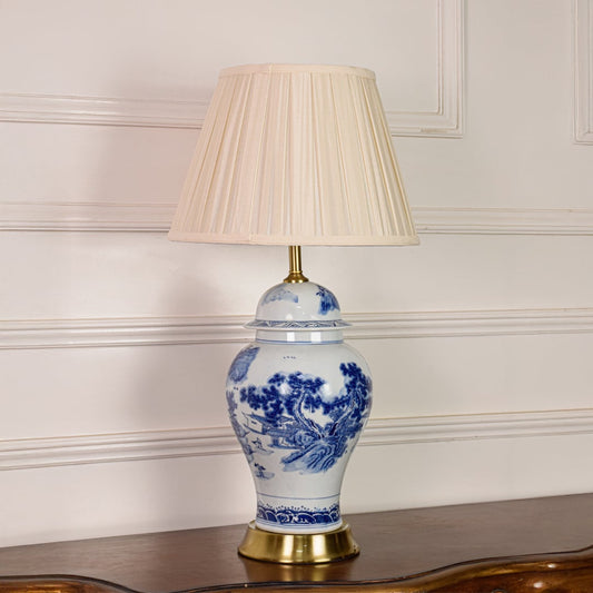 Blue and white ceramic table lamp shown unlit on white background featuring pleated fabric shade and classic porcelain base.
