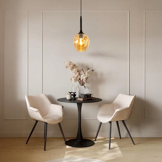 Amber glass pendant light hanging above dining table with beige chairs for modern home decor.