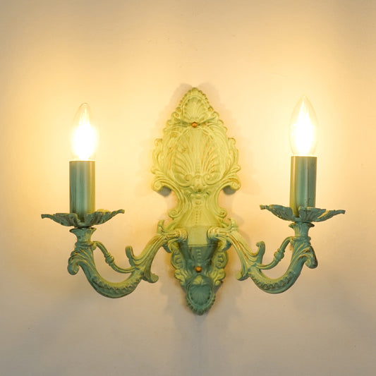 White background image of illuminated distressed green cast aluminium wall sconce for elegant rustic living room styling.