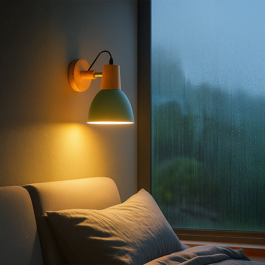 Modern wall light with matte green shade wooden base and black cord glowing warmly beside bed for cozy bedroom wall lighting.