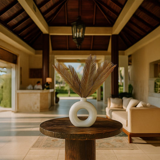 White ceramic round vase with dried golden palm leaves placed on wooden table in elegant modern living room decor.
