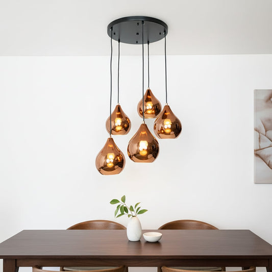 Modern copper pendant cluster with five glossy teardrop shades hanging from a black ceiling plate creating a warm elegant focal point in the room.