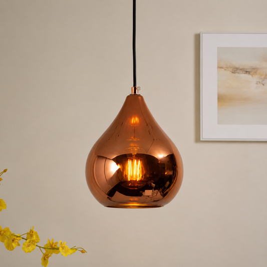A teardrop-shaped copper glass pendant light hanging from a black cord against a beige wall, with a framed print and yellow flowers partially visible in the background.