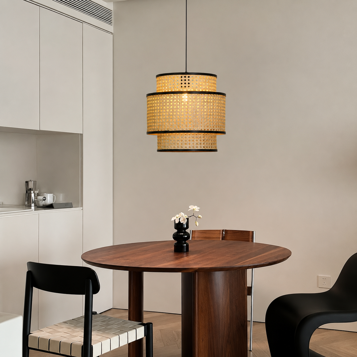 A modern two-tier cylindrical pendant light with a woven natural rattan shade and black metal trim, hanging over a round wooden dining table in a minimalist dining room.