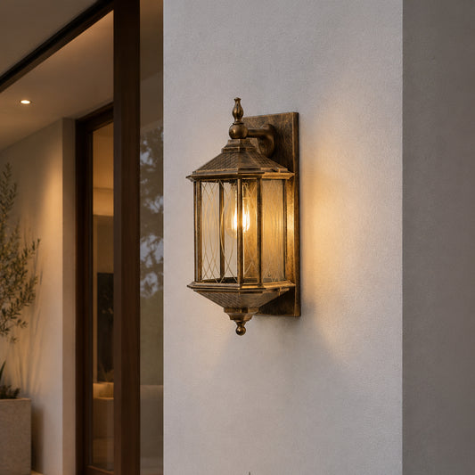 Antique brass metal outdoor wall light lifestyle image with a clear paneled glass lantern on a modern concrete wall.