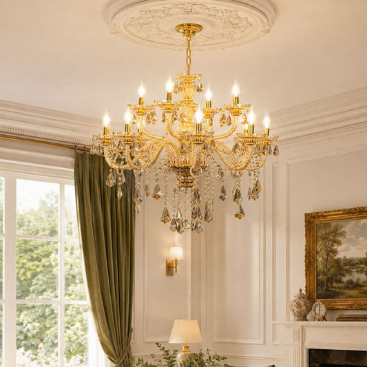 An ornate gold chandelier with hanging crystal prisms is installed in a classic room with white paneled walls, a window with green curtains, and a fireplace mantel.