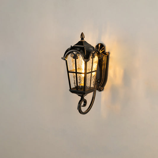 Black metal outdoor wall light on white background featuring a bottom scroll arm and paneled glass shade for patio decor.