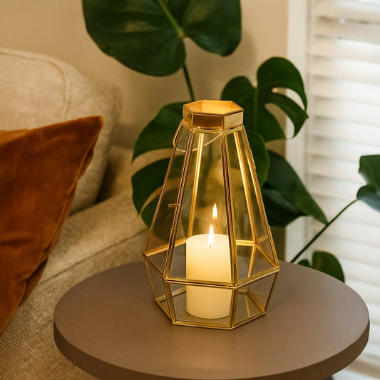 Decorative gold glass candle holder placed on a round side table beside a sofa styled with warm lighting and indoor green plants.