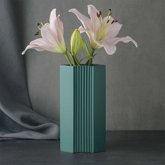 Ceramic flower vase in matte teal finish featuring vertical ribbed texture holding fresh pink lilies against a dark modern backdrop.