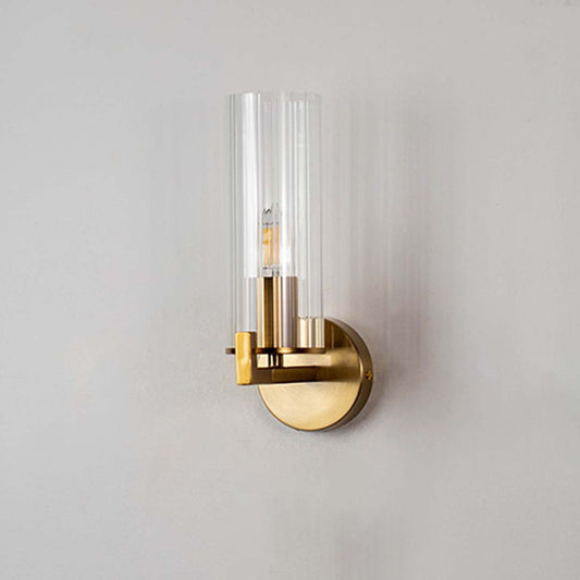 A tall ribbed glass shade wall sconce with a gold base shown against a clean white background with the light turned off.