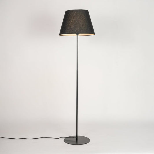 Black floor lamp illuminated through dark grey shade casting soft warm glow against white backdrop.
