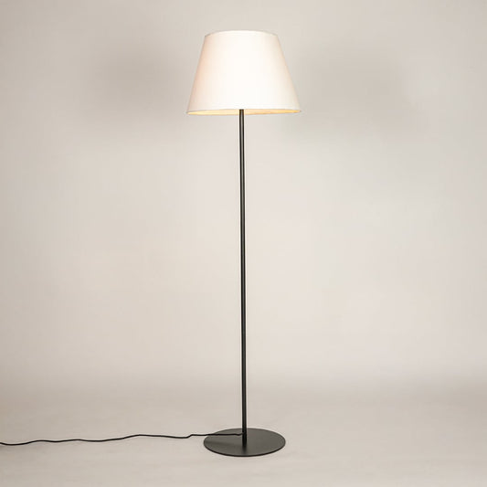 Black metal floor lamp glowing warmly through white fabric shade on white background for cozy home Decor.