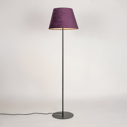 Black floor lamp illuminated through purple fabric shade creating cozy warm glow against white backdrop.