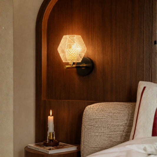 Luxury geometric clear glass wall sconce light on dark wooden headboard panel for elegant master bedroom interior styling.