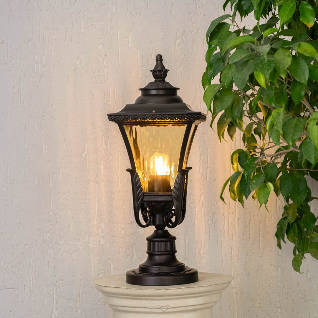 Black metal outdoor post lantern with clear glass placed on exterior pillar casting warm light ideal for garden entrance and pathway decor.
