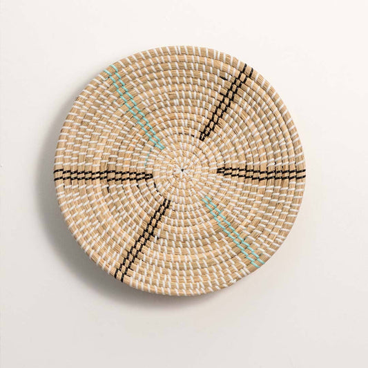 Round handcrafted natural cream seagrass wall basket with black and teal radial spoke patterns on white background.