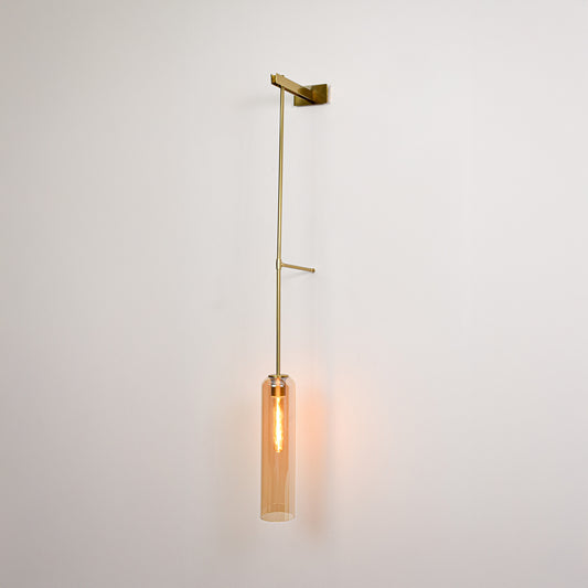 Gold metal wall light with hanging tube shade emitting warm ambient glow ideal for bedroom or hallway wall decor.