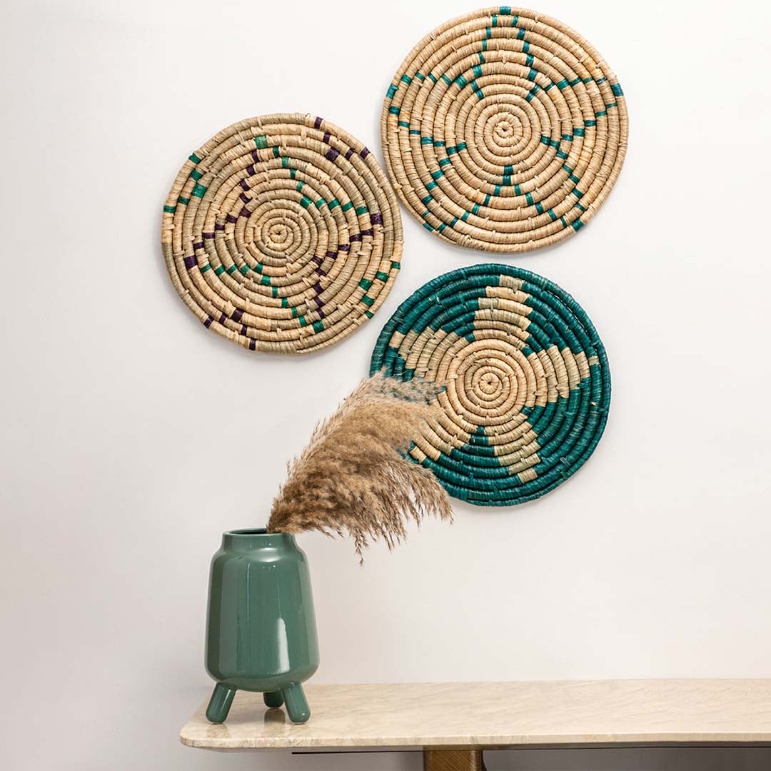 Set of three natural seagrass wall plates with geometric patterns arranged on a wall above a marble table for bohemian living room styling.