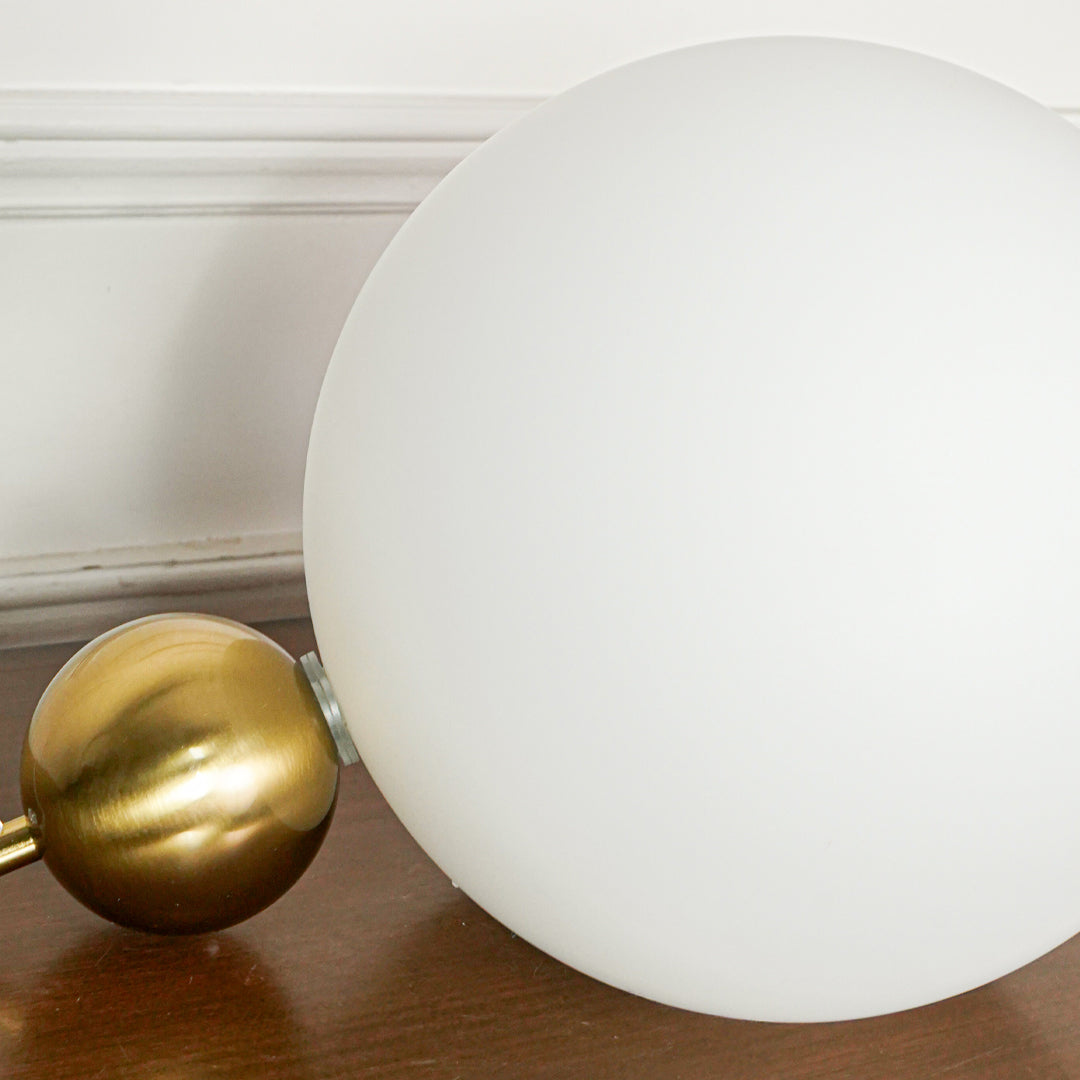 Minimal close up white glass globe lamp with smooth finish placed on wooden surface with gold decor accent and soft wall background for luxury styling.