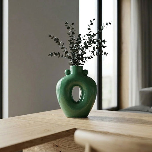 Green ceramic decorative flower vase placed on wooden table with leaves modern home decor styling idea.