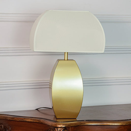 Minimal gold metal table lamp with curved base and frosted glass shade placed on soft off white background.