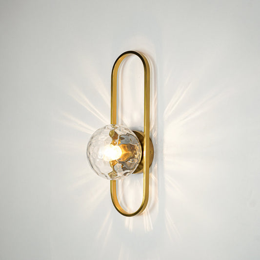Gold finish wall light with clear sculpted glass shade emitting warm glow ideal for elegant bedroom or hallway wall decor placement.
