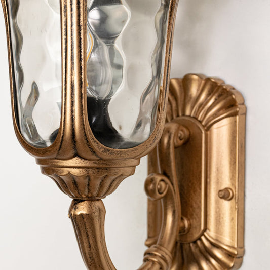Closeup of small gold metal outdoor wall lamp showing refined finish sturdy build and elegant detailing for exterior wall lighting use