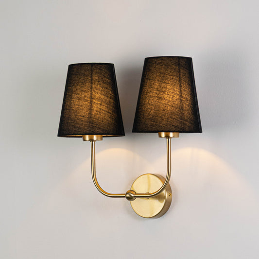 Elegant wall light in gold metal finish with dual dark fabric shades for bedroom or living decor lighting white background.