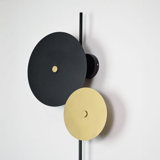 Wall light closeup highlighting layered circular discs with warm backlighting and contrasting matte black gold and white finishes for a sculptural design effect.