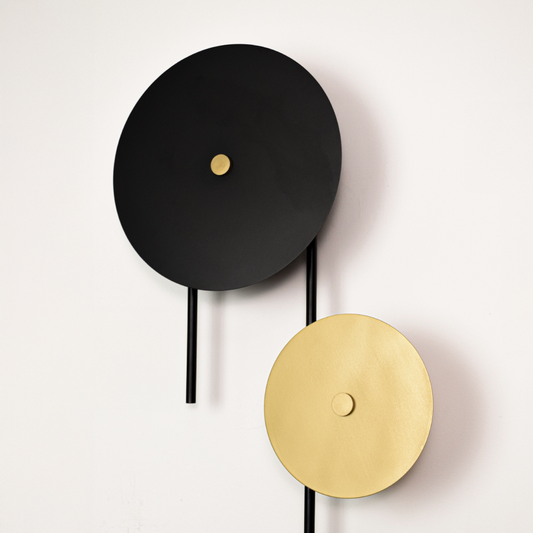 Closeup of modern wall light showing matte black rod with layered round discs in black gold and white highlighting premium finish and sculptural design.