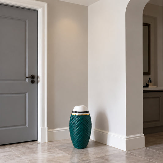 A decorative teal ceramic drum vase with a textured chevron pattern, a white top, and gold band accents, placed on a light stone tiled floor in a modern hallway.