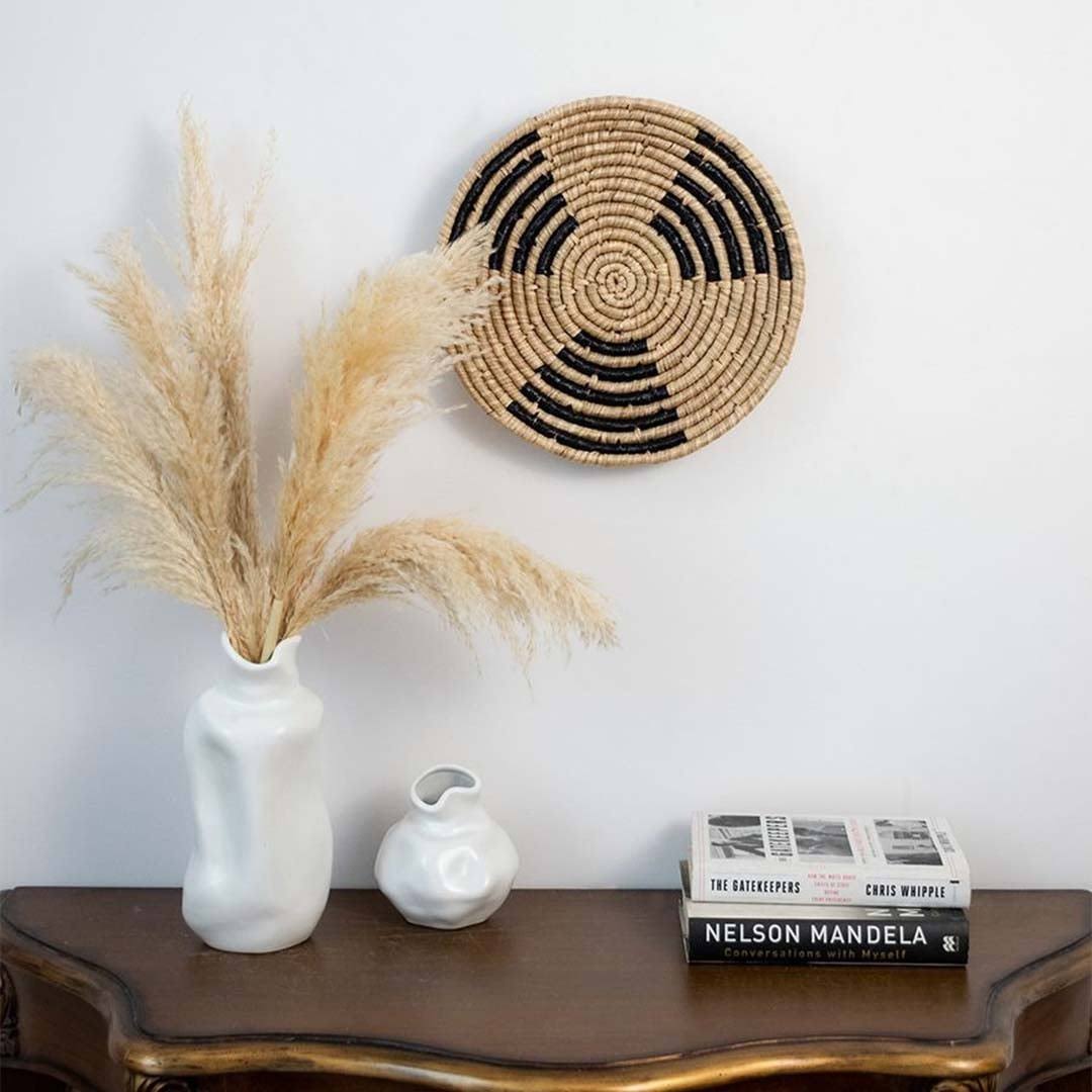 Handwoven seagrass wall basket decor in natural beige and black displayed above a console creating elegant boho home style.