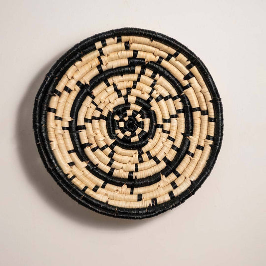 Round handcrafted black and cream woven seagrass wall basket with abstract concentric dash pattern on white background.