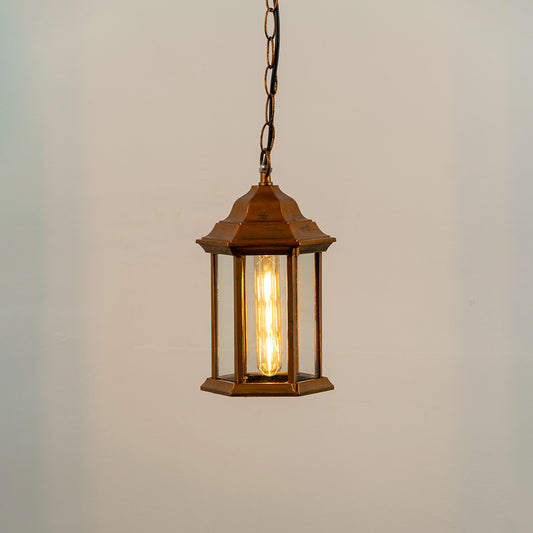 Copper metal hanging outdoor lantern with glass enclosure glowing on white background suitable for porch entrance and exterior decor lighting.