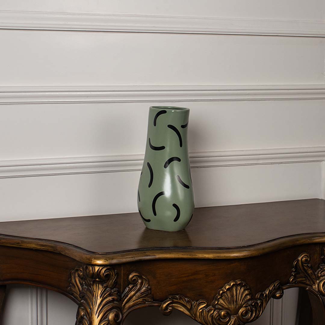 Matte green ceramic vase with black curved detailing shown on a white background highlighting its sculpted modern silhouette.
