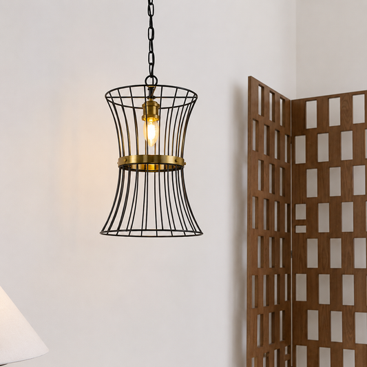 A black wire cage pendant light with a brass-colored middle band and a glowing bulb, hanging against a white wall next to a wooden folding screen.