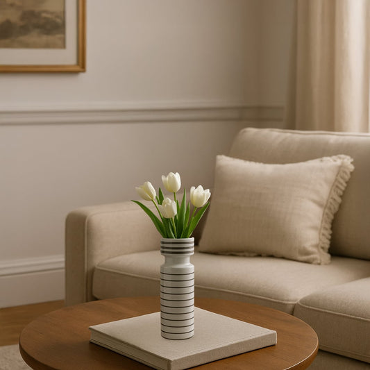 Striped white ceramic vase styled on wooden coffee table with fresh flowers creating calm modern living room decor accent.