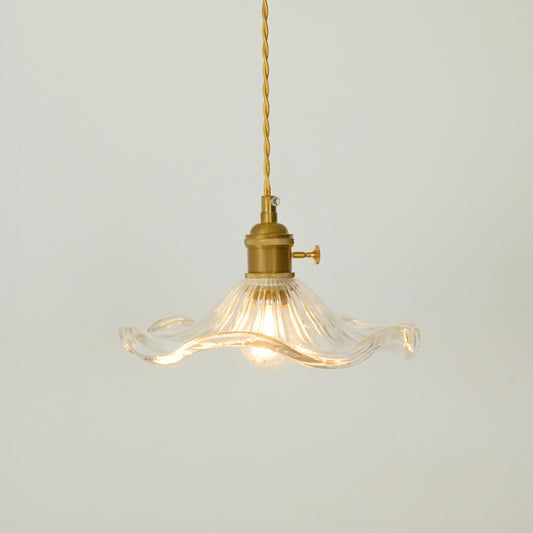 A vintage-style pendant light with a clear ribbed glass shade that has wavy, flared edges and a brass metal fixture, suspended from a brass cord against a light gray background.