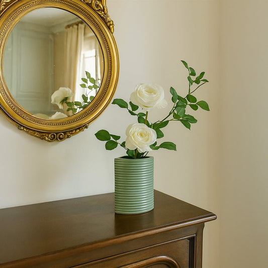 Green ceramic vase with ribbed texture holding white roses placed on a wooden console beneath a gold-framed mirror for an elegant decor setting.