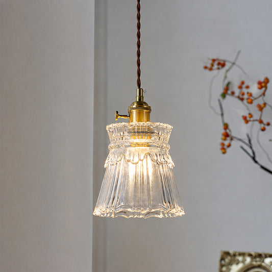 A vintage-style pendant light with a clear ribbed glass bell shade and a brass socket, hanging from a brown twisted cord against a light gray wall.