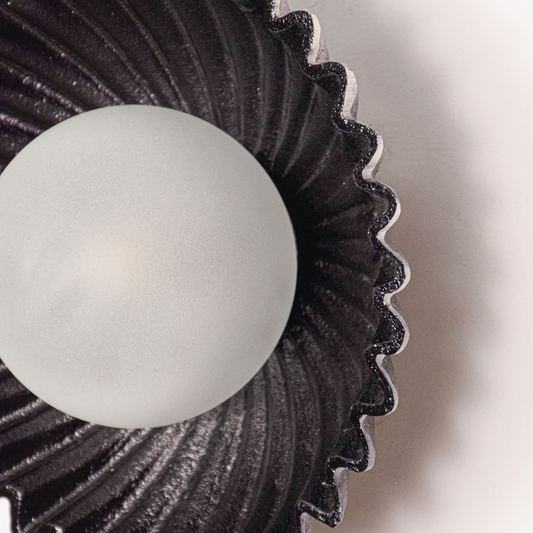 Wall light closeup reveals detailed textured metal finish sculpted circular form and softly diffused light creating a refined premium look.