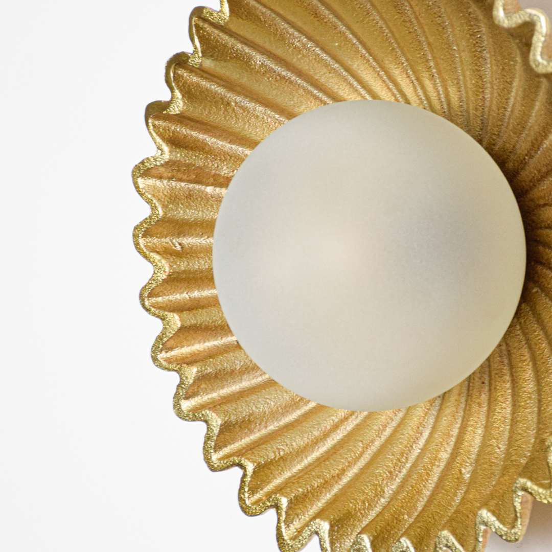 Wall light closeup highlighting rippled gold metal texture with smooth frosted glass globe showcasing premium craftsmanship and elegant finish.