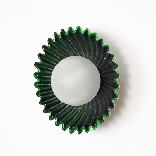 Wall light off on white background featuring deep green fluted metal plate with centered glass globe for minimalist product presentation.