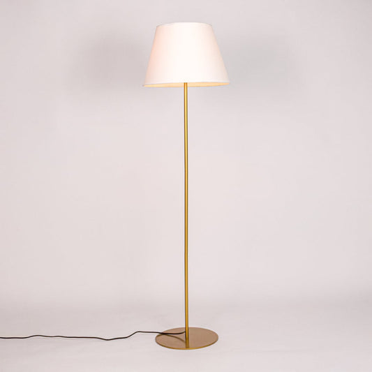 Gold floor lamp illuminated with warm glow through white fabric shade against minimal white studio background.