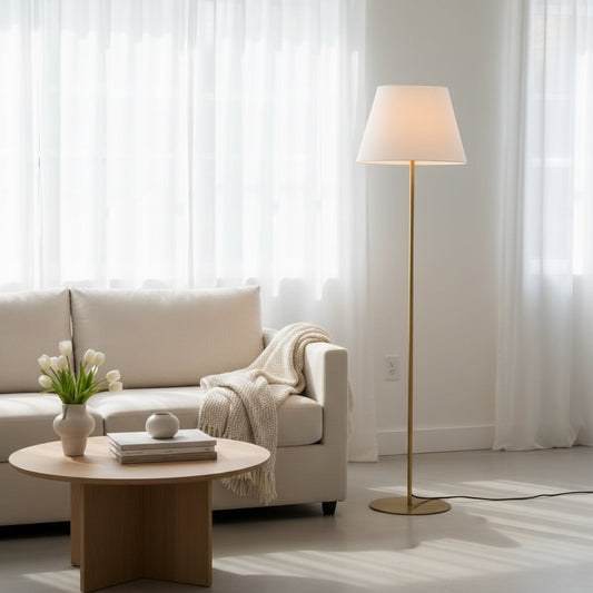Elegant gold floor lamp with wide white fabric shade styled beside sofa in bright modern living room interior setting.