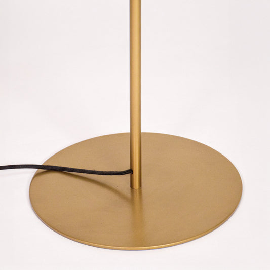 Round gold metal base with slim vertical stand and visible black power cord detail on white background.