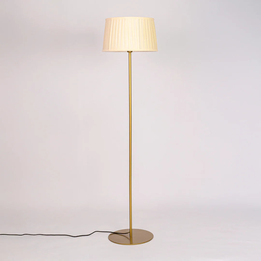 Gold metal floor lamp with pleated white shade displayed against clean white background with light turned off.